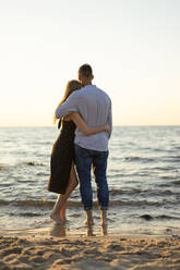 Romantisches junges Paar, das sich umarmt und vom Strand aus auf den Horizont blickt - SSGF00327