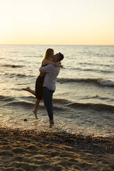 Romantic man lifting and kissing woman on beach at sunset - SSGF00329