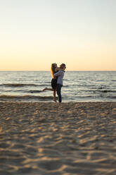 Man lifting woman on beach at sunset - SSGF00330