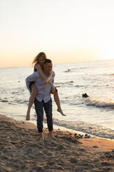 Playful woman piggybacking on man at beach - SSGF00332