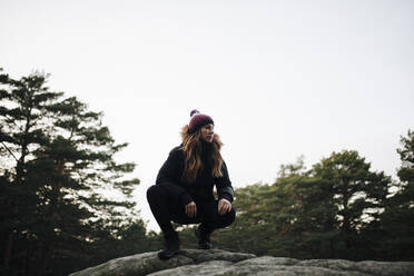 Woman crouching on rock in forest - MRRF01692