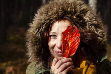 Frau bedeckt Gesicht mit Herbstblatt im Wald - MRRF01722