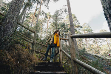Woman in coat moving down on steps in forest - MRRF01725
