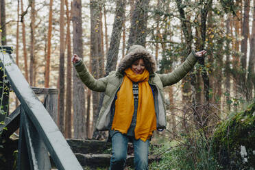 Happy woman with arms outstretched moving down on steps in forest - MRRF01727