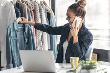 Modedesigner, der ein Hemd hält und mit einem Handy im Büro telefoniert - JSRF01699