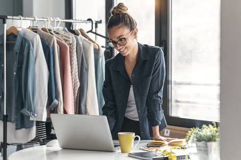 Lächelnde Modedesignerin mit Laptop im Büro - JSRF01704