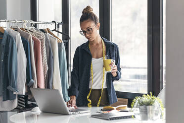 Modedesigner mit Kaffeetasse und Laptop im Büro - JSRF01705