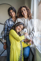 Girl embracing dog by mother and sister at home - DLTSF02420