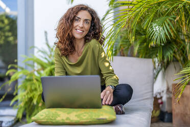 Frau mit Laptop auf einem Liegestuhl auf der Terrasse sitzend - DLTSF02422