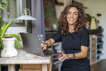 Smiling woman with laptop at home - DLTSF02438