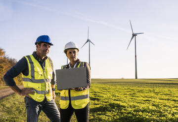 Ingenieur mit Laptop im Gespräch mit einem Kollegen im Windpark - UUF25070