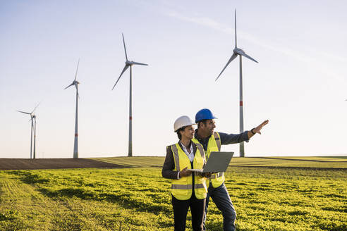 Engineer explaining to colleague with laptop at wind park - UUF25072