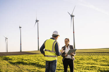 Ingenieur erklärt einem lächelnden Kollegen mit digitaler Tafel an einem sonnigen Tag - UUF25074