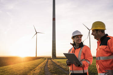 Ingenieure mit Schutzhelmen diskutieren bei Sonnenuntergang - UUF25095