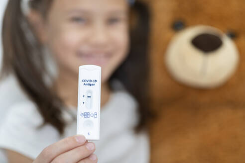 Lächelndes Mädchen mit Teddybär, das das Ergebnis eines diagnostischen Schnelltests zeigt - DRF01782