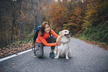 Smiling woman kneeling with dog on road - OMIF00182