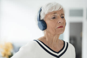 Senior woman listening music through wireless headphones at home - JOSEF05923