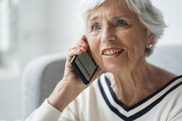 Lächelnde Frau, die zu Hause mit ihrem Smartphone telefoniert - JOSEF05926