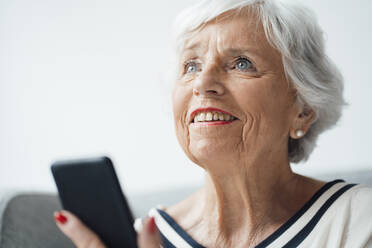 Lächelnde ältere Frau mit Smartphone zu Hause - JOSEF05931
