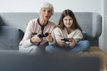 Grandmother playing video game with granddaughter at home - JOSEF05947