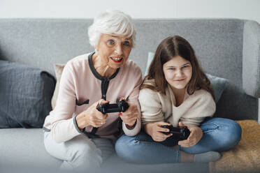 Grandmother playing video game with granddaughter at home - JOSEF05979