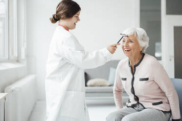 Playful girl checking woman with reflex hammer at home - JOSEF05983