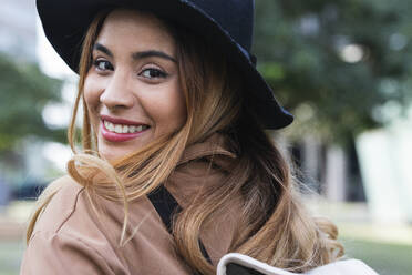 Smiling blond woman wearing hat looking over shoulder - PNAF02574