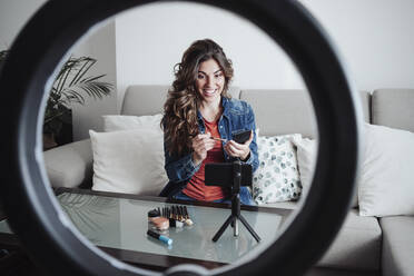 Smiling influencer with make-up palette influencing at home studio - EBBF04867