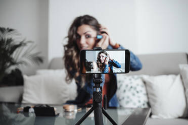 Vlogger applying mascara and influencing through smart phone at home studio - EBBF04874