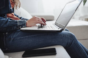 Young woman using laptop on sofa at home - EBBF04892