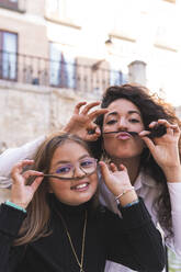 Mother and daughter making mustache with hair - JAQF00952