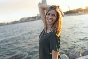 Lächelnde Frau mit Hand im Haar am Strand von Bogatell, Barcelona, Katalonien, Spanien - JSRF01710