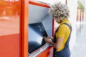 Woman with afro hairstyle using ATM machine - XLGF02402