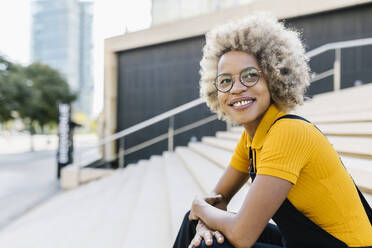 Smiling woman with eyeglasses sitting on steps - XLGF02408