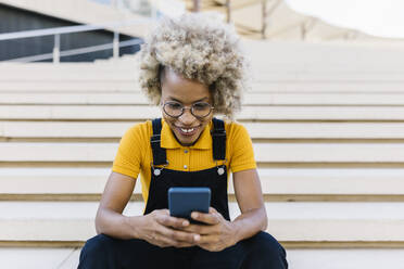 Frau mit Brille benutzt Mobiltelefon auf einer Treppe - XLGF02411