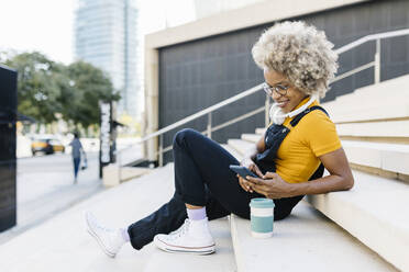 Woman with headphones using mobile phone on steps - XLGF02414