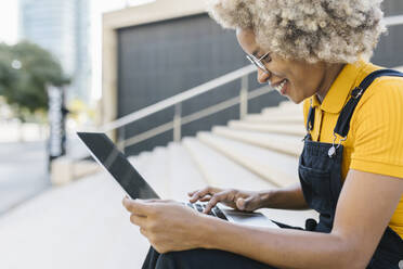 Smiling woman using laptop on steps - XLGF02418