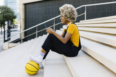 Woman with basketball using mobile phone on steps - XLGF02428