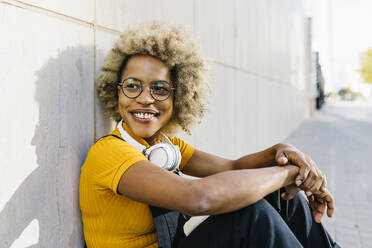Frau mit Brille und Kopfhörern sitzt vor einer Wand - XLGF02430