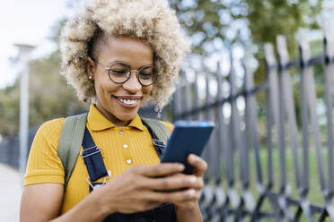 Lächelnde Frau mit Brille, die ein Mobiltelefon benutzt - XLGF02451