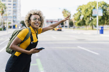 Smiling woman with mobile phone gesturing on road - XLGF02454