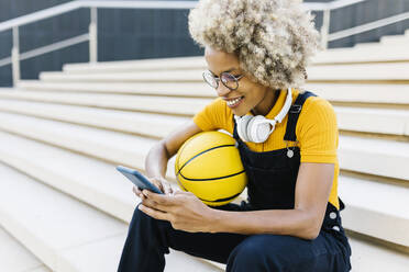 Lächelnde Frau mit Sportball und Mobiltelefon auf einer Treppe - XLGF02466