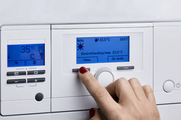 Woman adjusting control panel of heating boiler at home - ZEDF04287