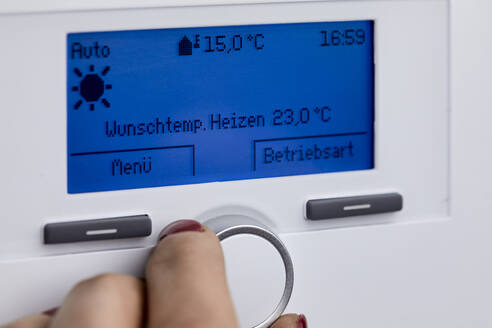Woman adjusting heating boiler with control knob at home - ZEDF04293