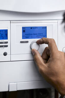 Man adjusting heating boiler with control knob at home - ZEDF04298
