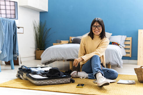 Junge Frau mit Brille packt Koffer im Schlafzimmer zu Hause - GIOF14230