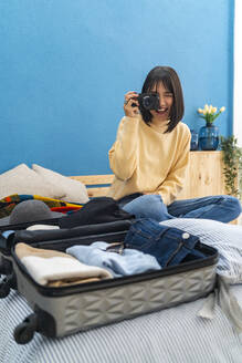 Glückliche junge Frau beim Fotografieren mit Kamera auf dem Bett zu Hause - GIOF14246