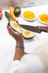 Woman slicing avocado with kitchen knife at home - JAQF00977