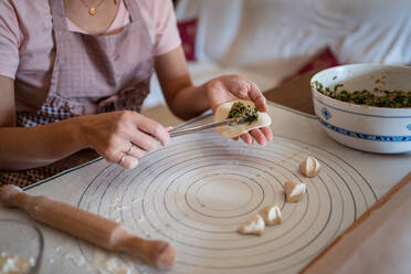 From above of crop unrecognizable woman in casual clothes and apron stuffing dumplings with meat while preparing traditional Chinese jiaozi in kitchen - ADSF31857