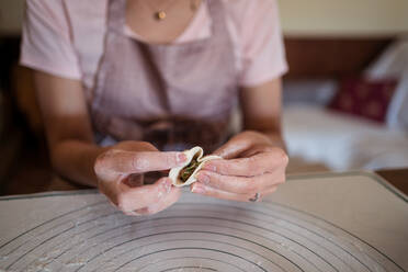 From above of crop unrecognizable woman in casual clothes and apron stuffing dumplings with meat while preparing traditional Chinese jiaozi in kitchen - ADSF31859